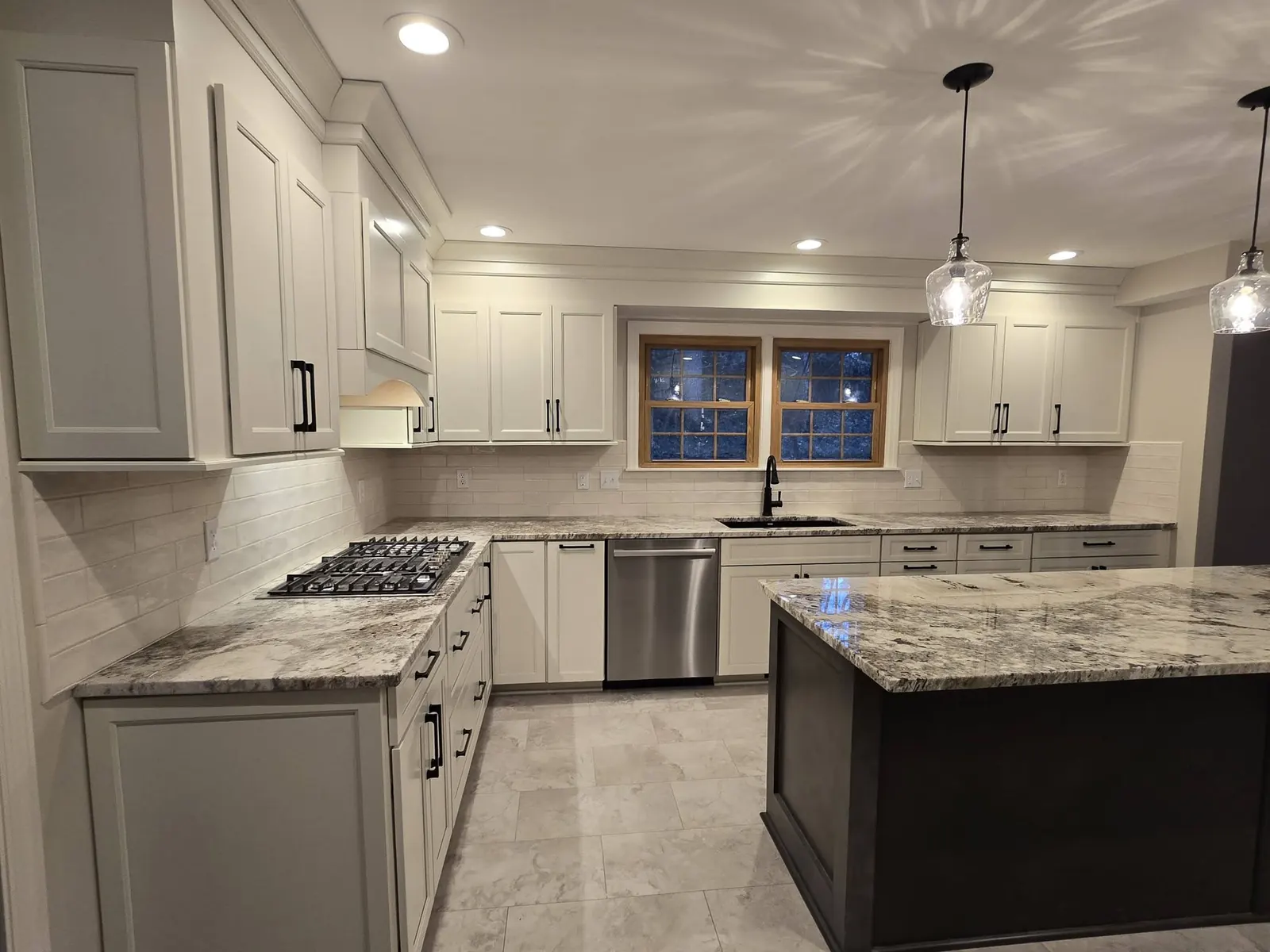 Finished kitchen remodel with white shaker cabinets, granite countertops, subway tile backsplash, and a dark island by Integrity Restorations and Remodeling