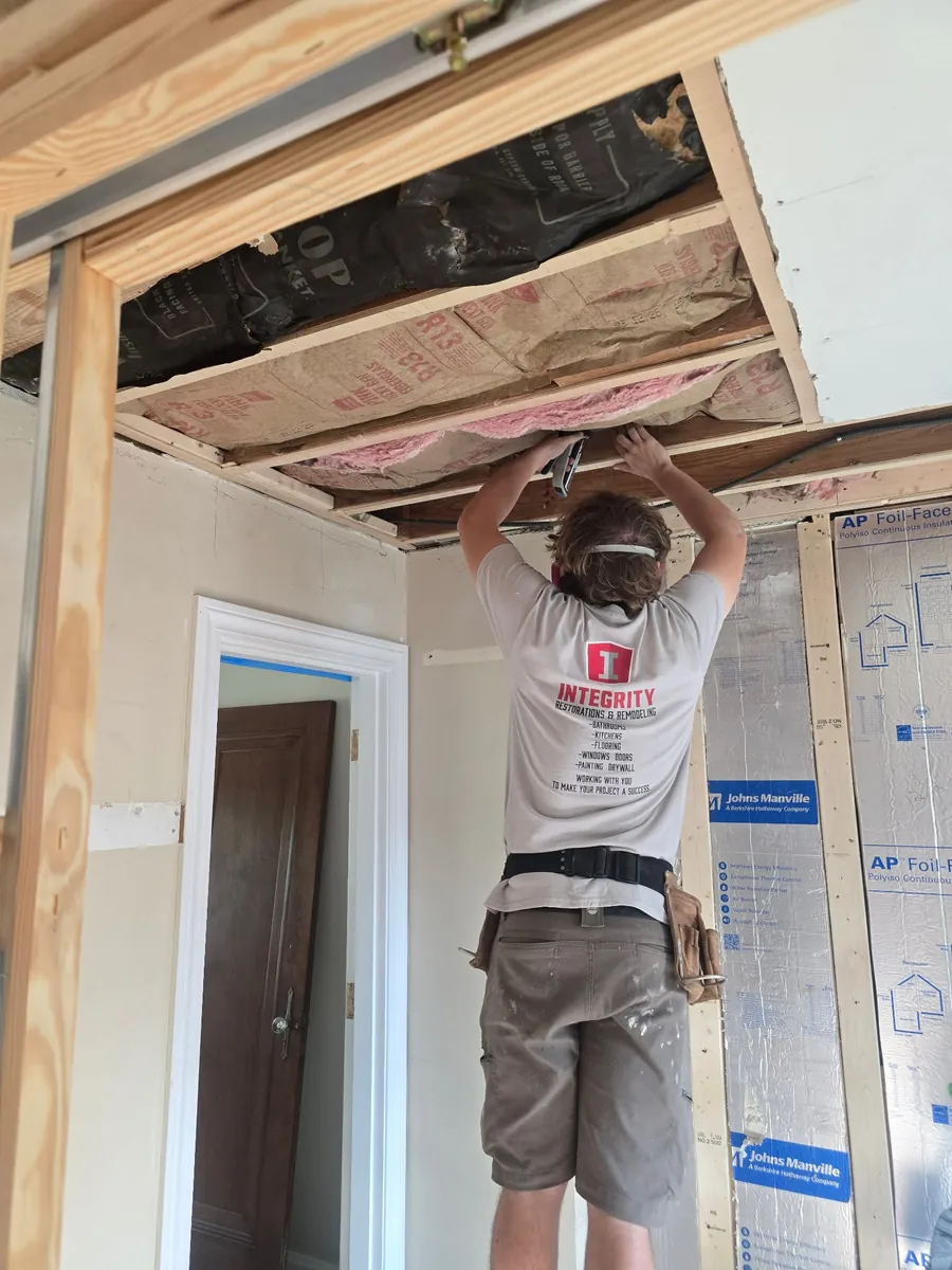 A crew member in an Integrity shirt fastening insulation into an open ceiling bay