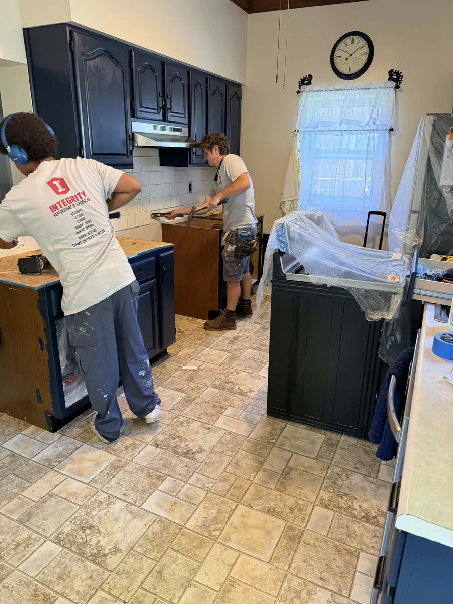 Two crew members at work in a kitchen with navy cabinets, one wearing an Integrity shirt