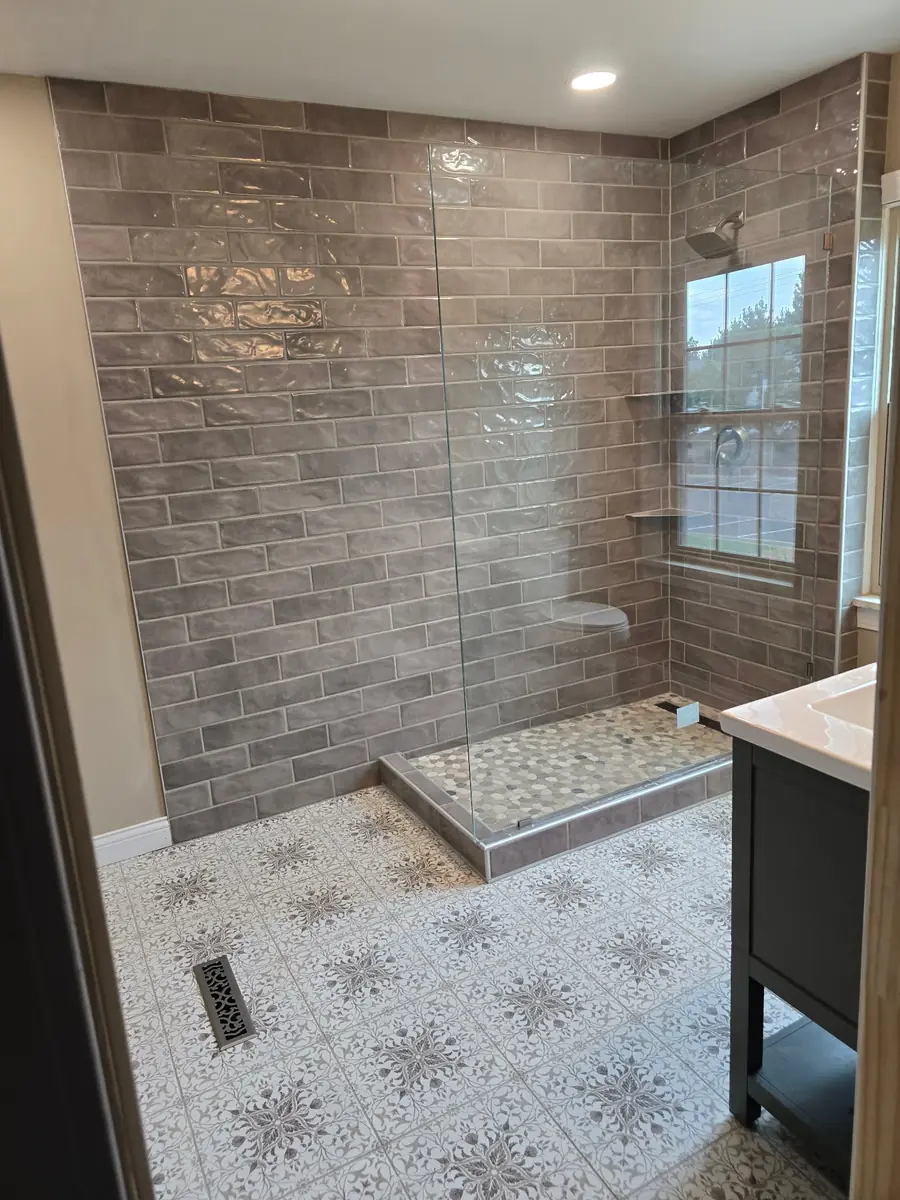 Same bathroom finished: a walk-in shower with grey subway tile, patterned floor tile and a new vanity