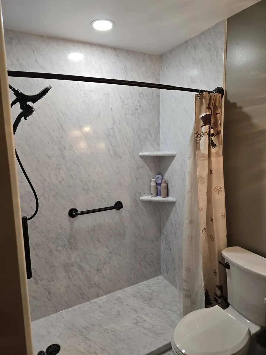Same bathroom after: a tiled walk-in shower with a glass door and a grab bar