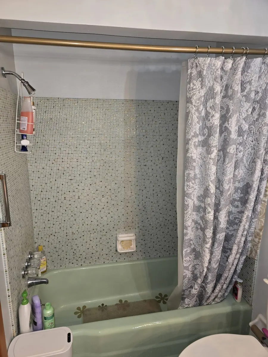 Dated tub and shower with a green tub, patterned tile and a shower curtain