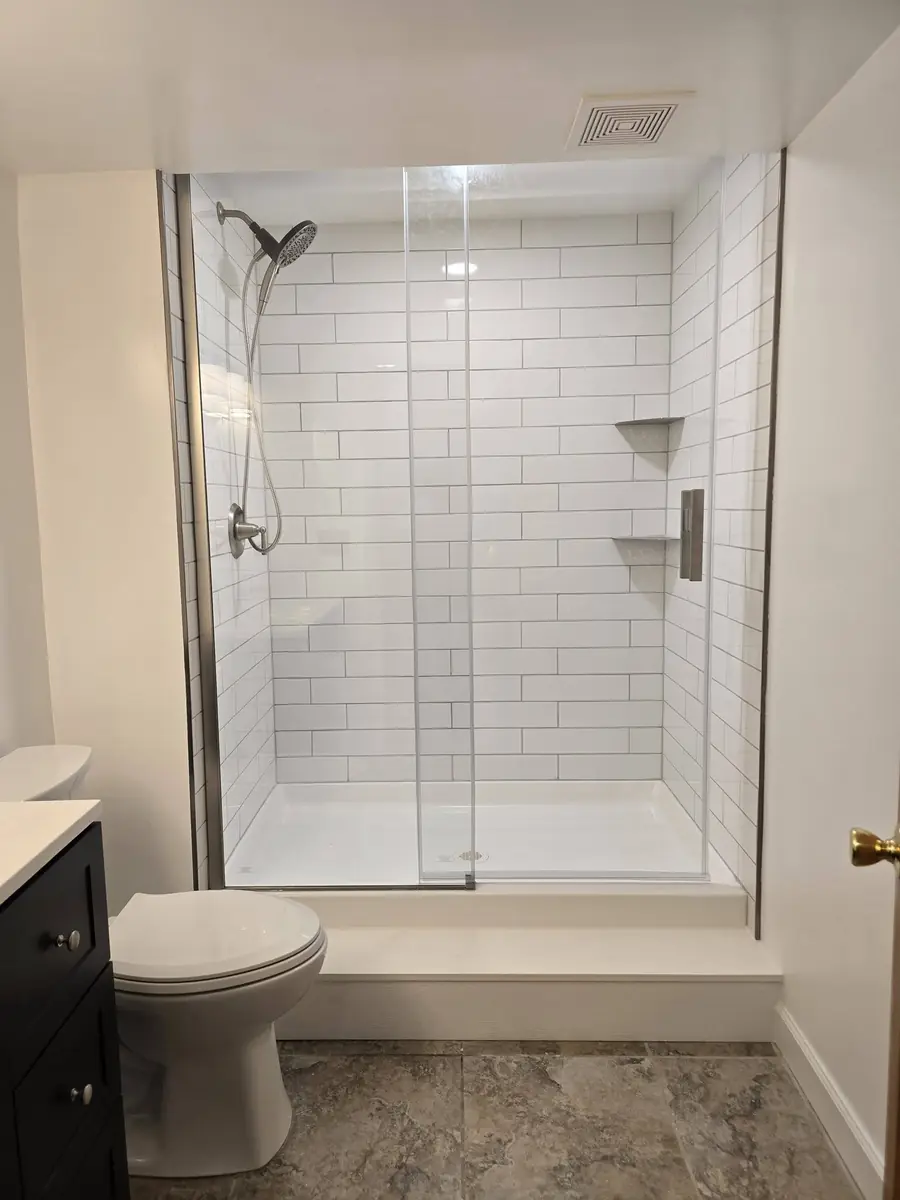 Same bathroom after: a white tile walk-in shower with a glass door and a new vanity