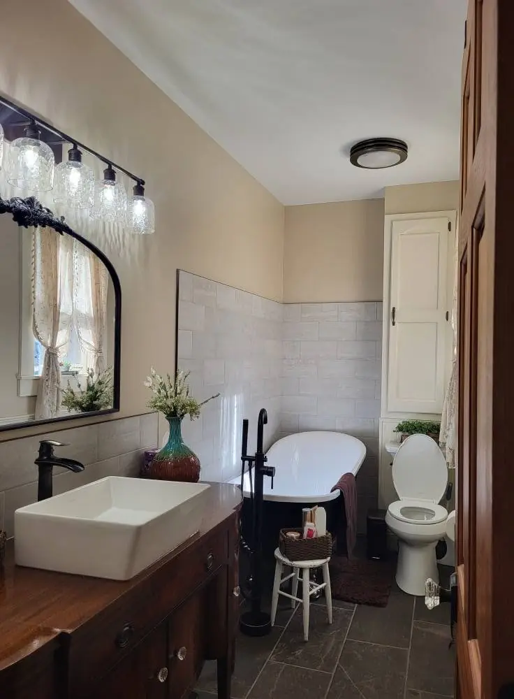 Same bathroom after: a vessel sink on a new vanity, a black mirror and lighting, and new flooring