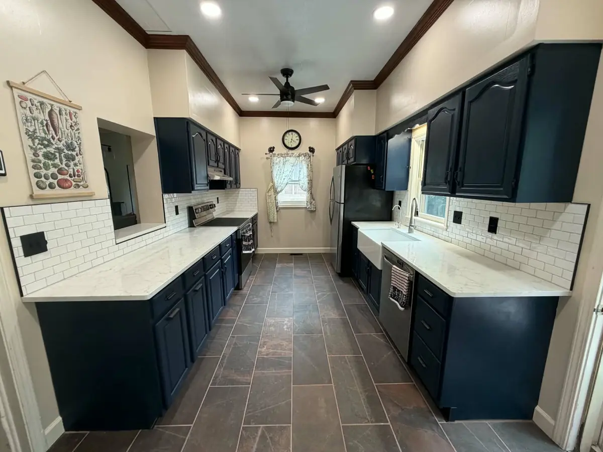 Same kitchen after remodel: navy cabinets, white countertops, white subway tile and new wood-look flooring