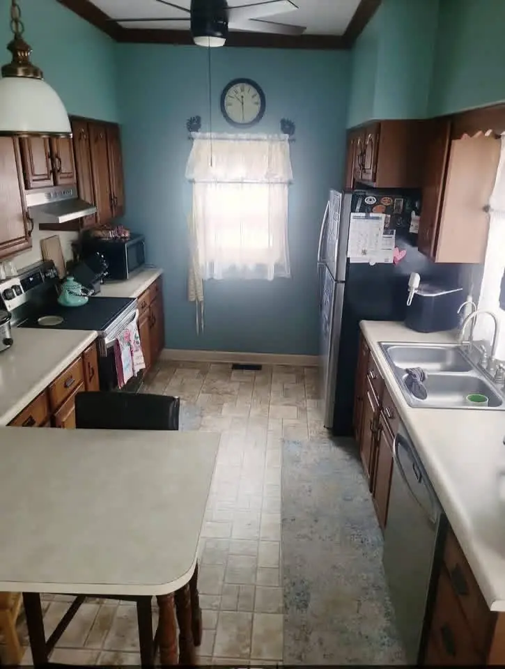 Galley kitchen before remodel: oak cabinets, teal walls and a small window over the sink